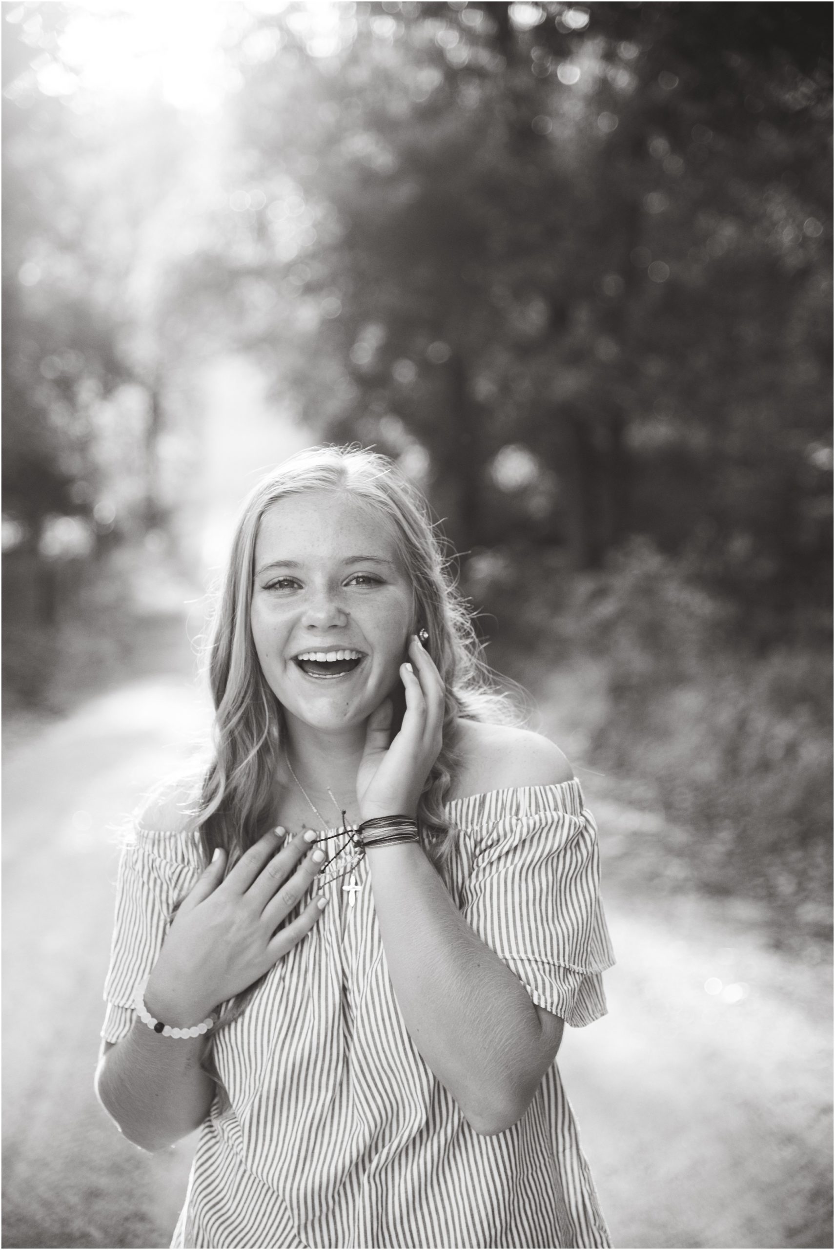 black and white image of senior girl laughing on gravel road in off the shoulder shirt for senior session