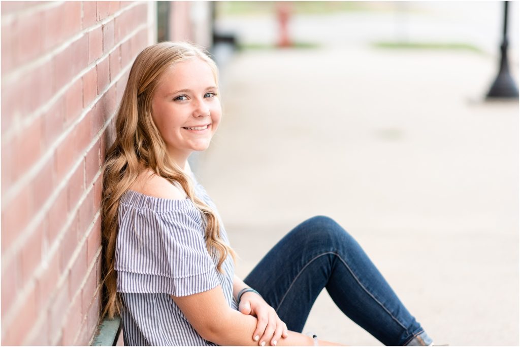 blonde girl leaning against brick wall smiling at camera for senior session