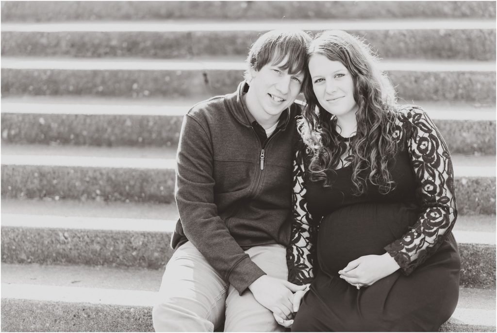 black and white image of expecting couple sitting on stairs smiling at camera