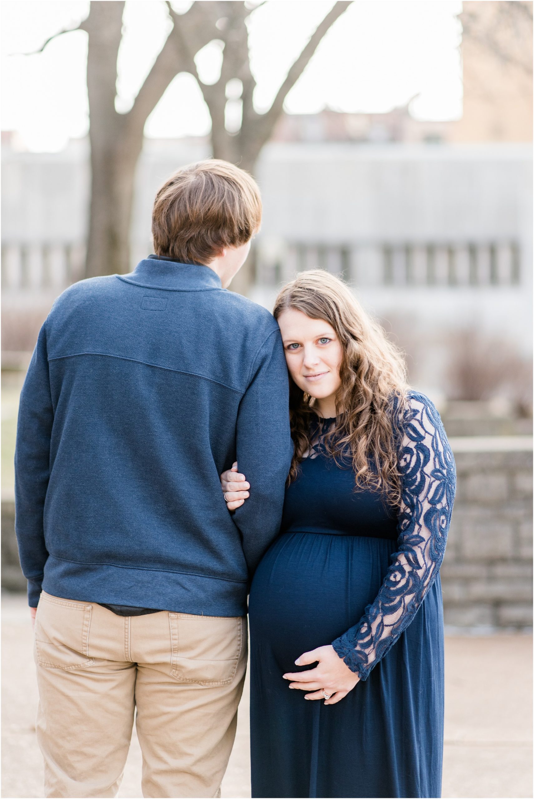 maternity session with couple wearing navy clothing and wife holding her belly and looking at camera