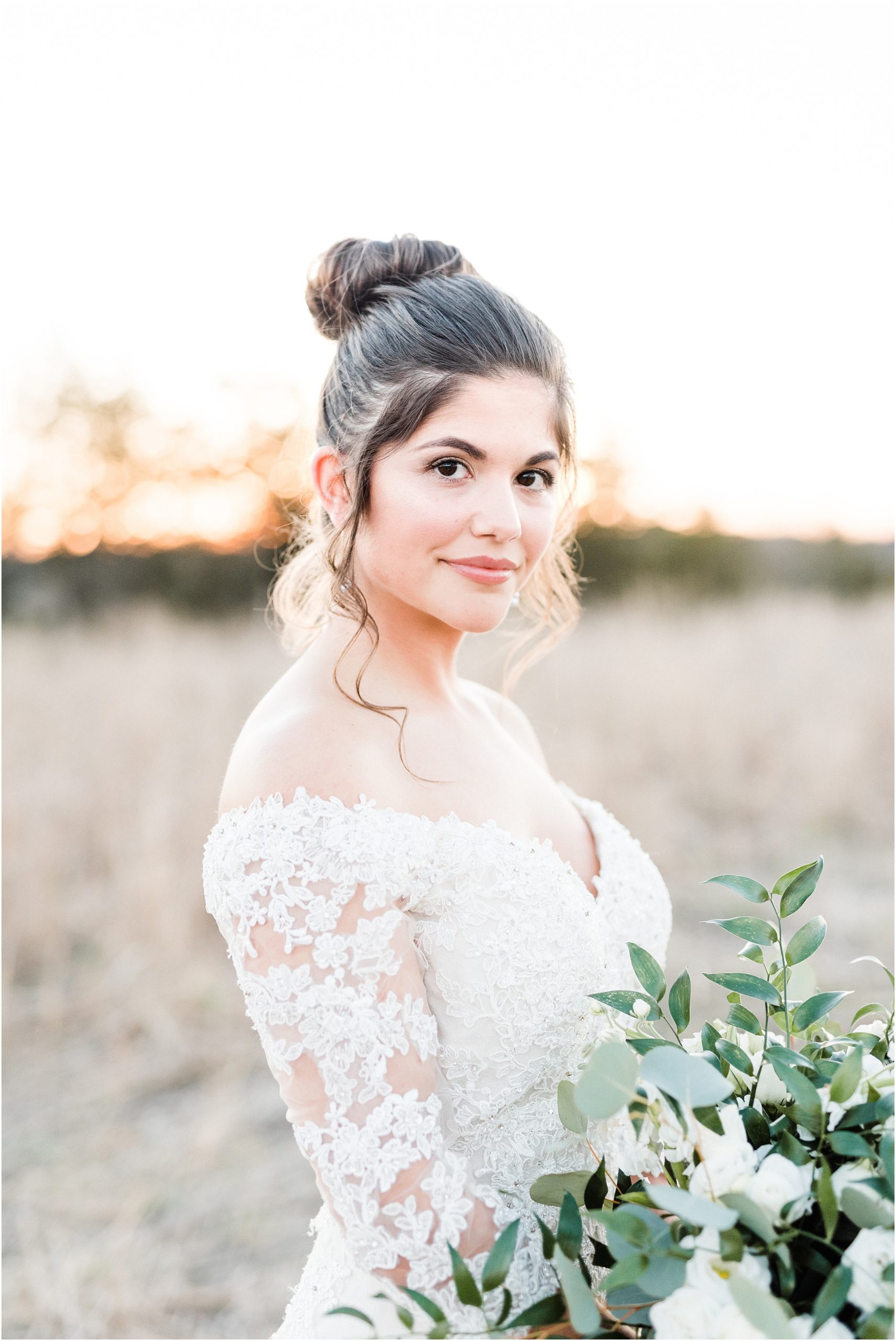 bride with brown hair up in bun staring at camera with off the shoulder wedding dress and green and white bouquet for dreamy bridal session