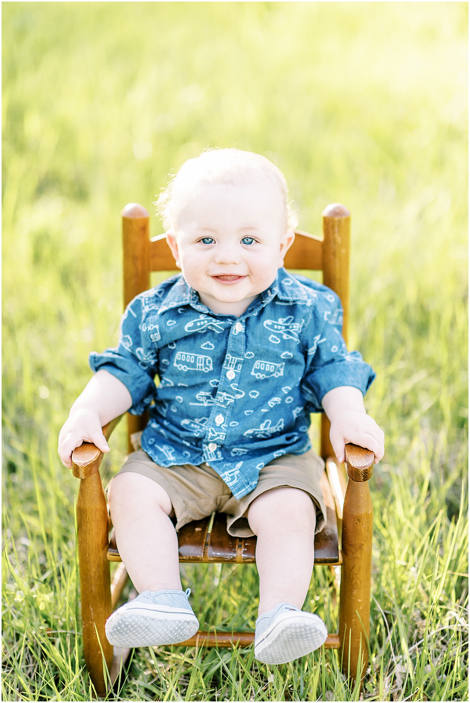 one year old boy in blue sitting on wooden rocking chair in tall grass