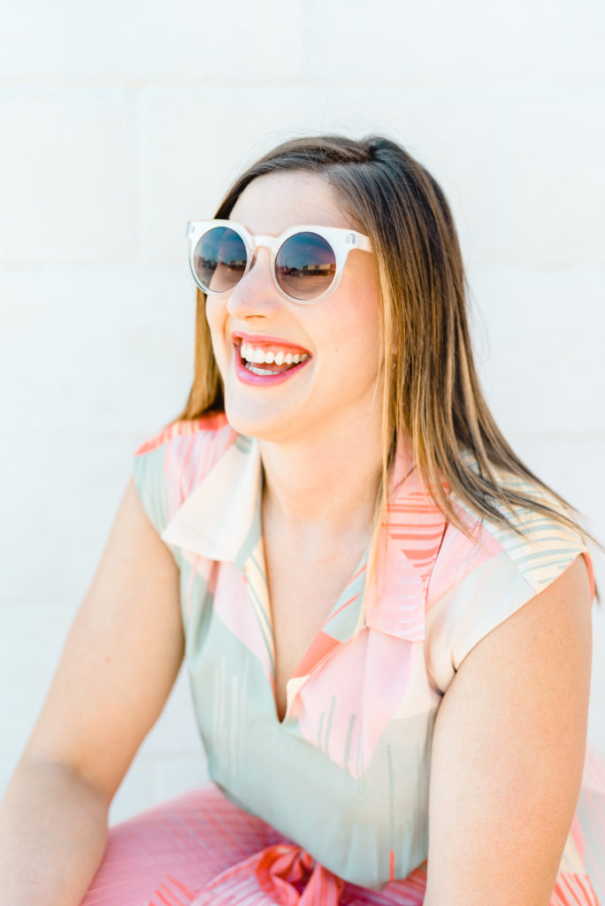 Terra Nickelson smiles broadly while wearing funky white sunglasses for a headshot