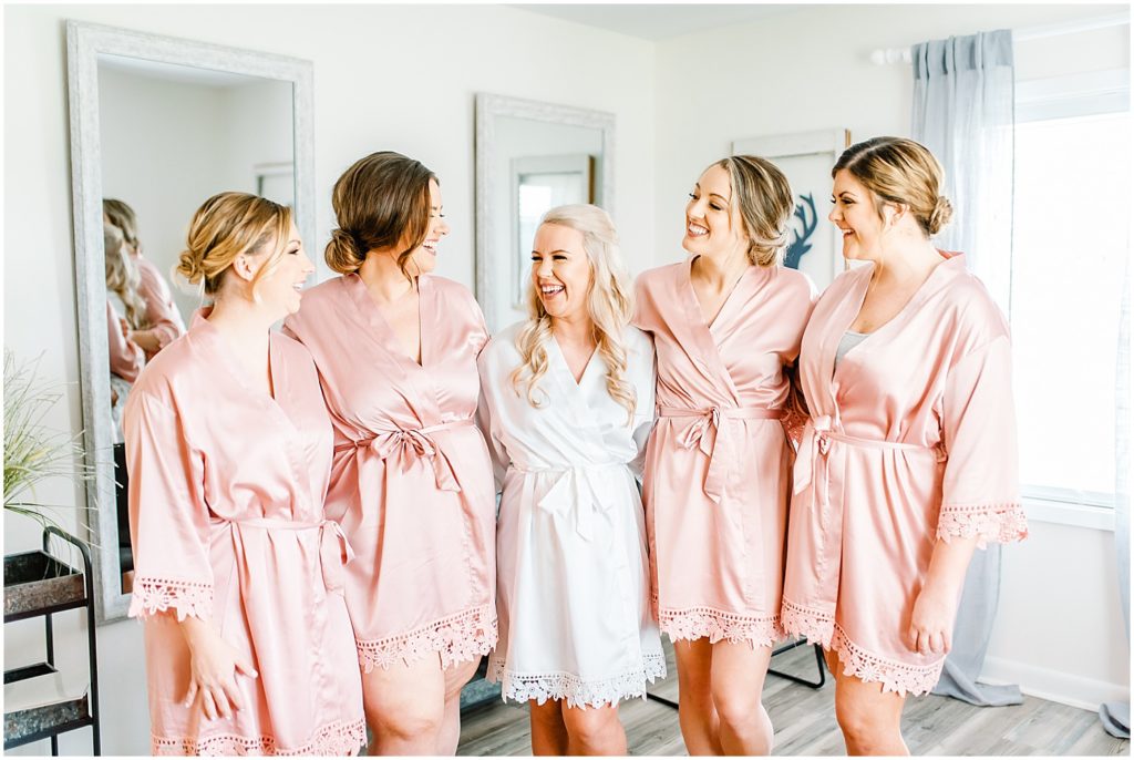 bride and bridesmaids in pink robes smiling for camera in getting ready room
