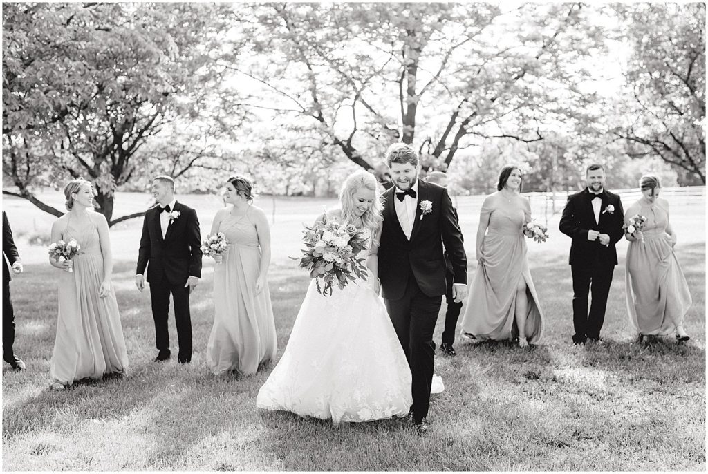 black and white image of bride and groom walking with wedding party outside cooper's ridge