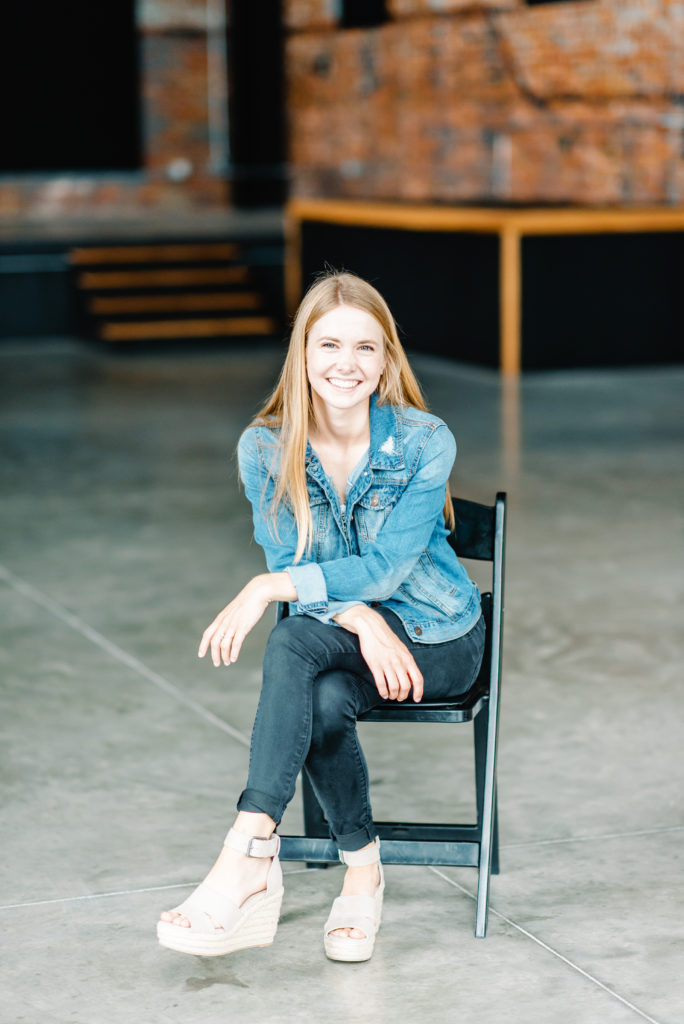 woman in jean jacket sitting on black chair in empty wedding event venue