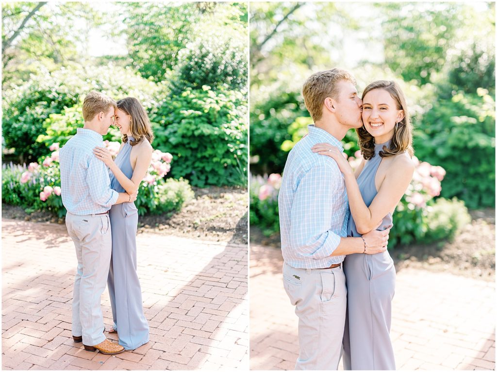 engaged couple kissing in front of flower bed and greenery for pictures