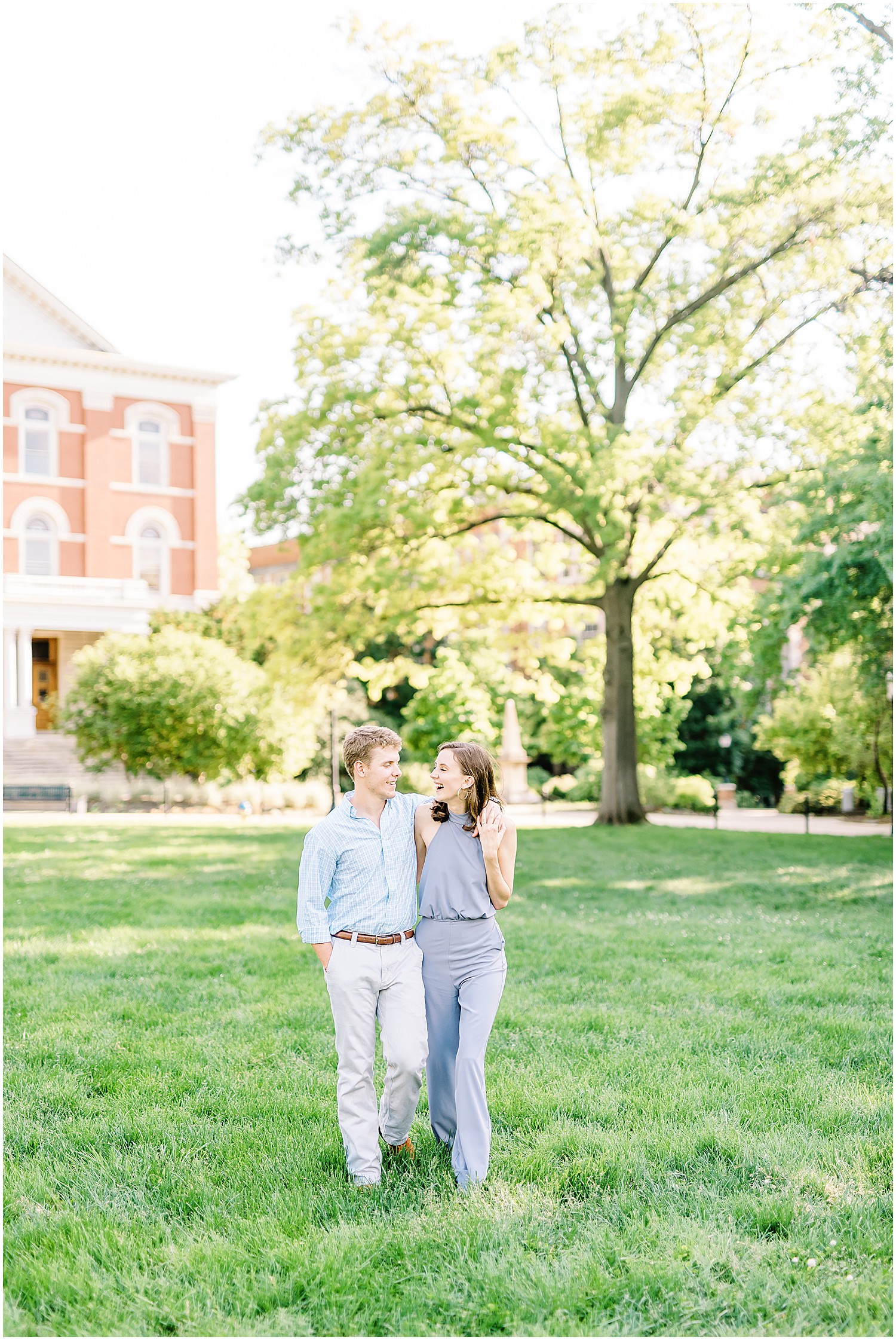 couple walks on the lawn with large tree in the background in columbia, mo for engagement pictures