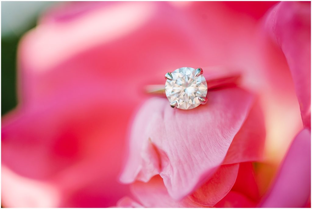 up close image of engagement ring sitting in bright pink flower for engagement session