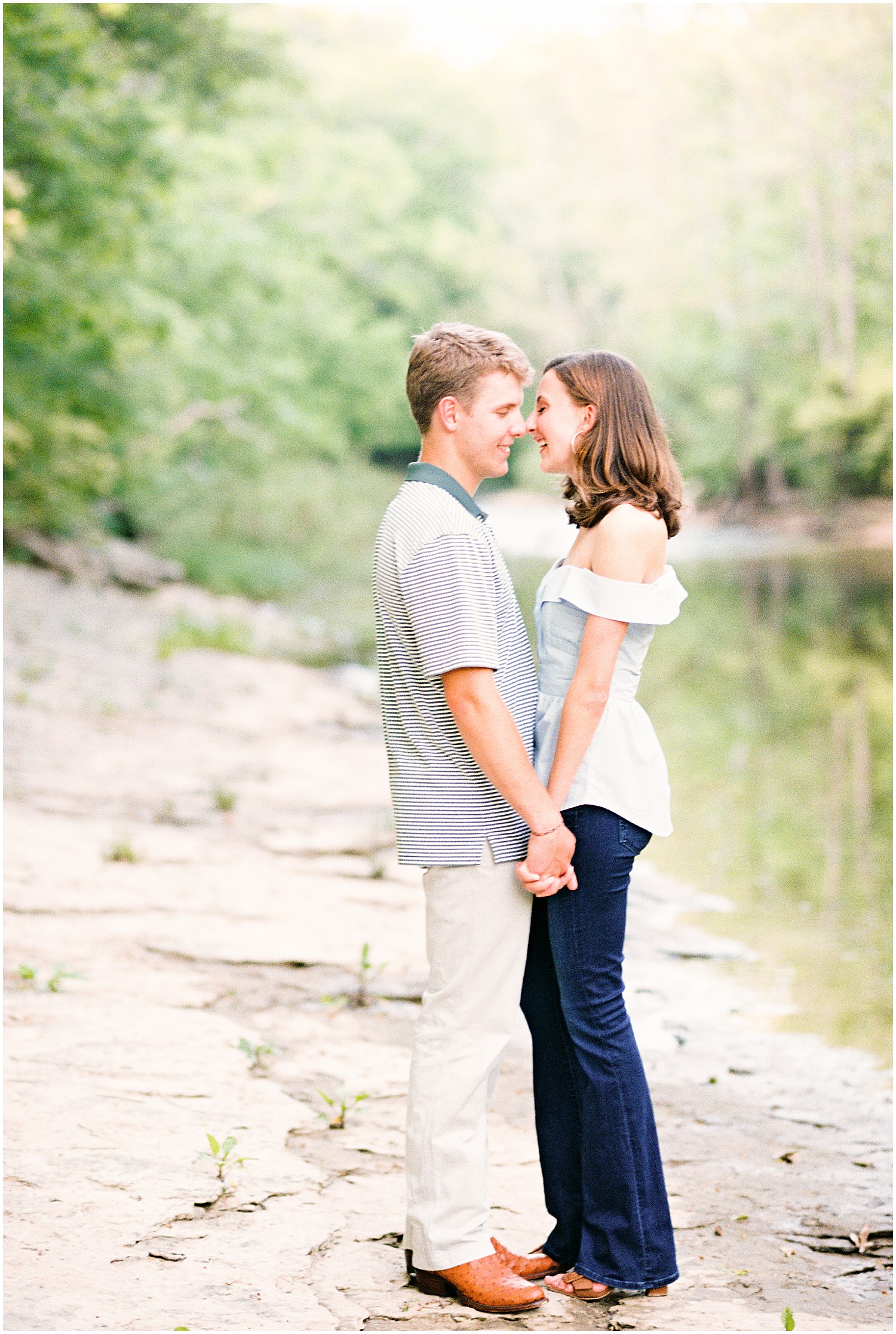 young couple stands on rocks in creek bed for capen park engagement session in columbia, mo
