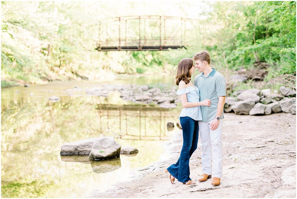 couple kisses in front of bridge in creek bed at capen park in columbia, mo