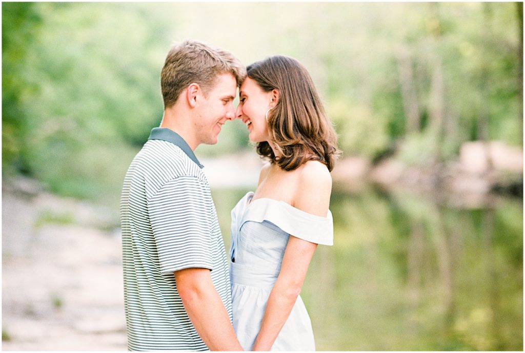 couple smiles and kisses in creek bed for engagement session