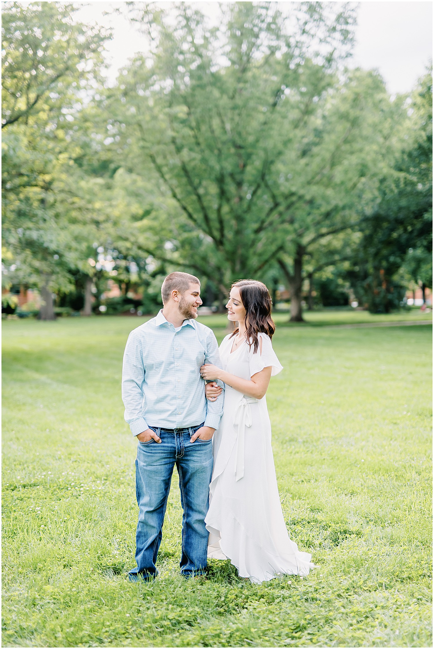 couple standing in grass lawn smiling at each other for engagement session