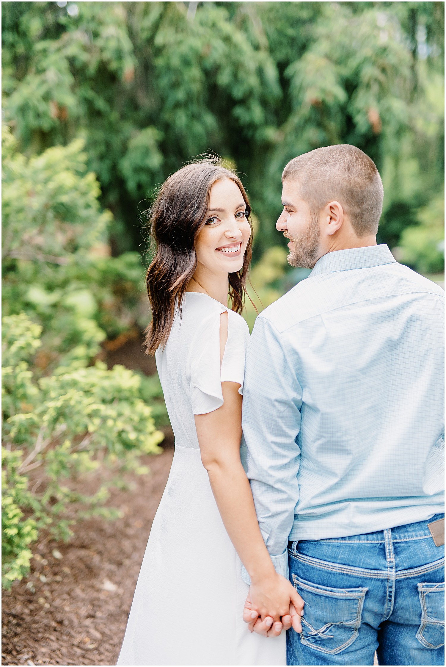 woman smiles back at camera as fiance smiles at her for engagement session at shelter gardens