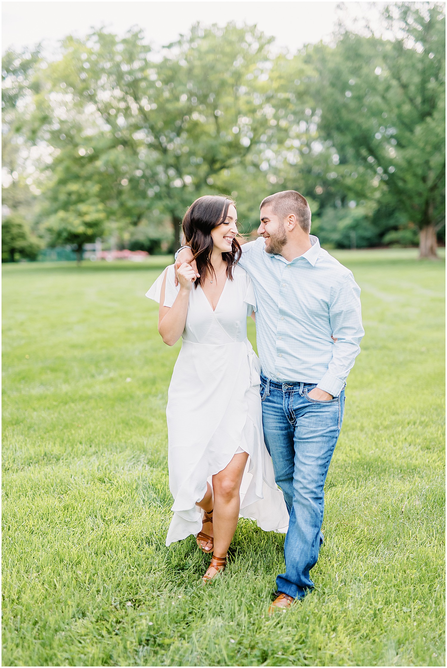 couple walks arm in arm through the grass for engagement pictures in shelter gardens