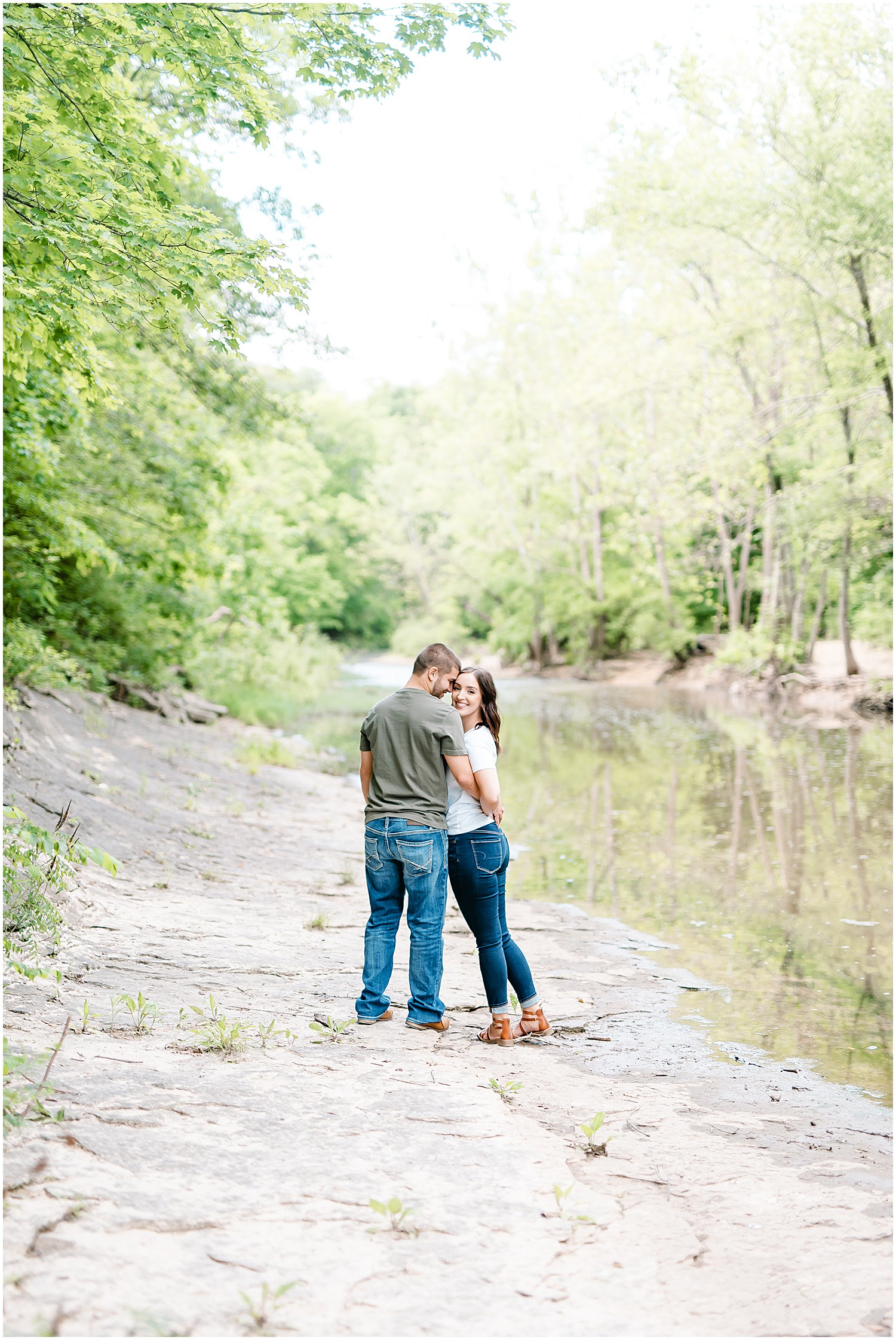 a couple stands next to the water in a creek bed for engagement session at capen park