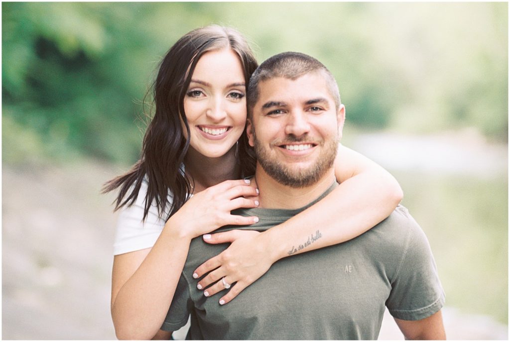 man and fiance smile at the camera while giving a piggy back ride for engagement session