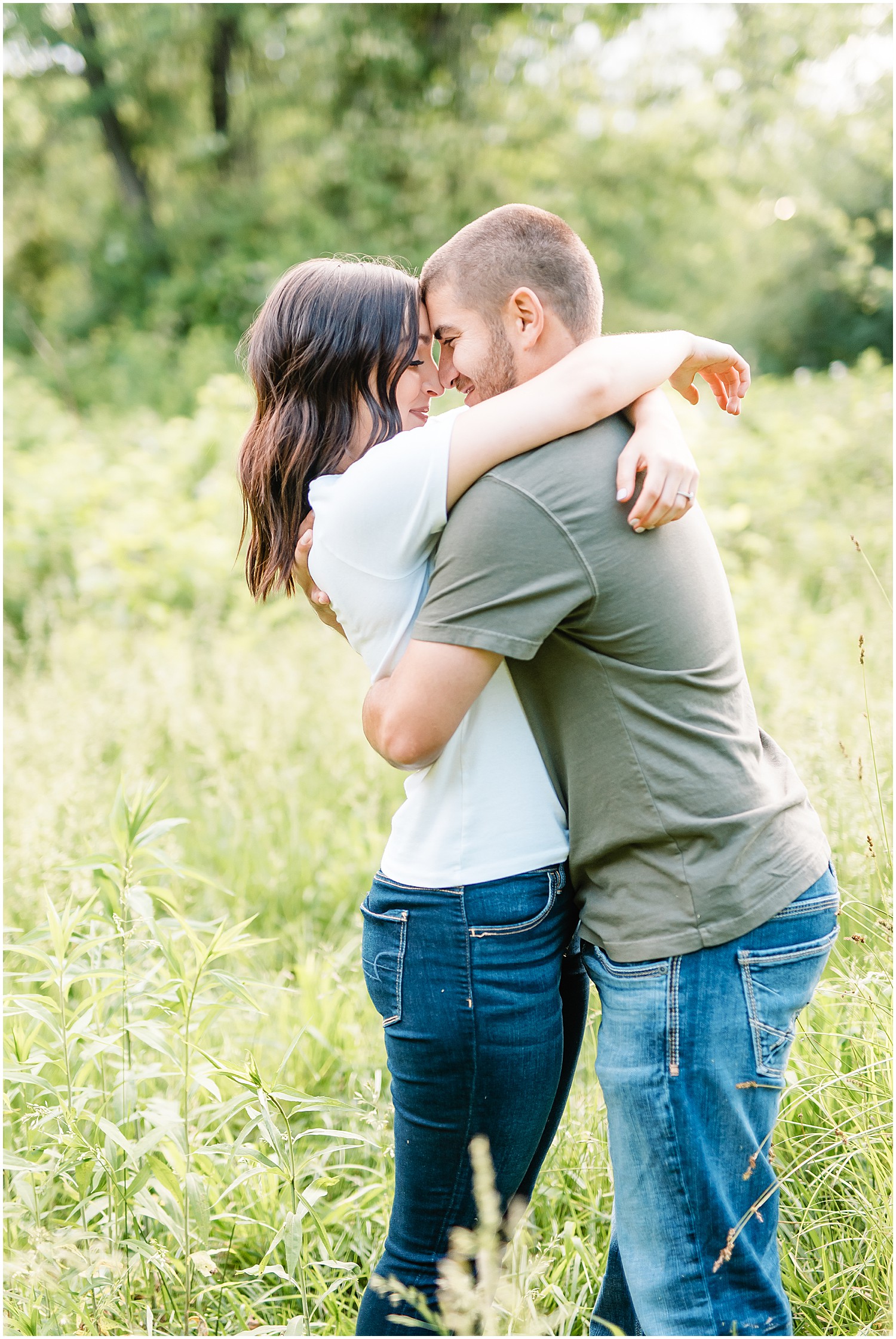 couple touches noses and holds each other in tall grass for engagement pictures