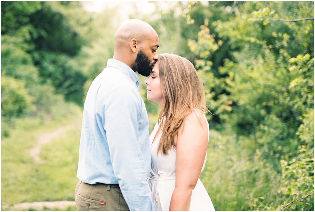 man kisses fiance on forehead during jefferson city engagement session at greenway surrounded by trees