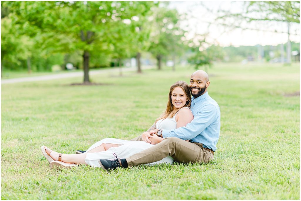 couple sits in grass and smiles for engagement session at park