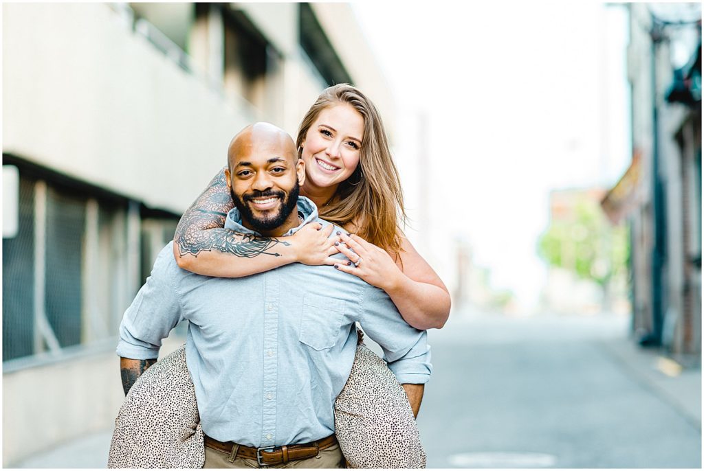 man gives fiancé piggy back ride in alley way during engagement session