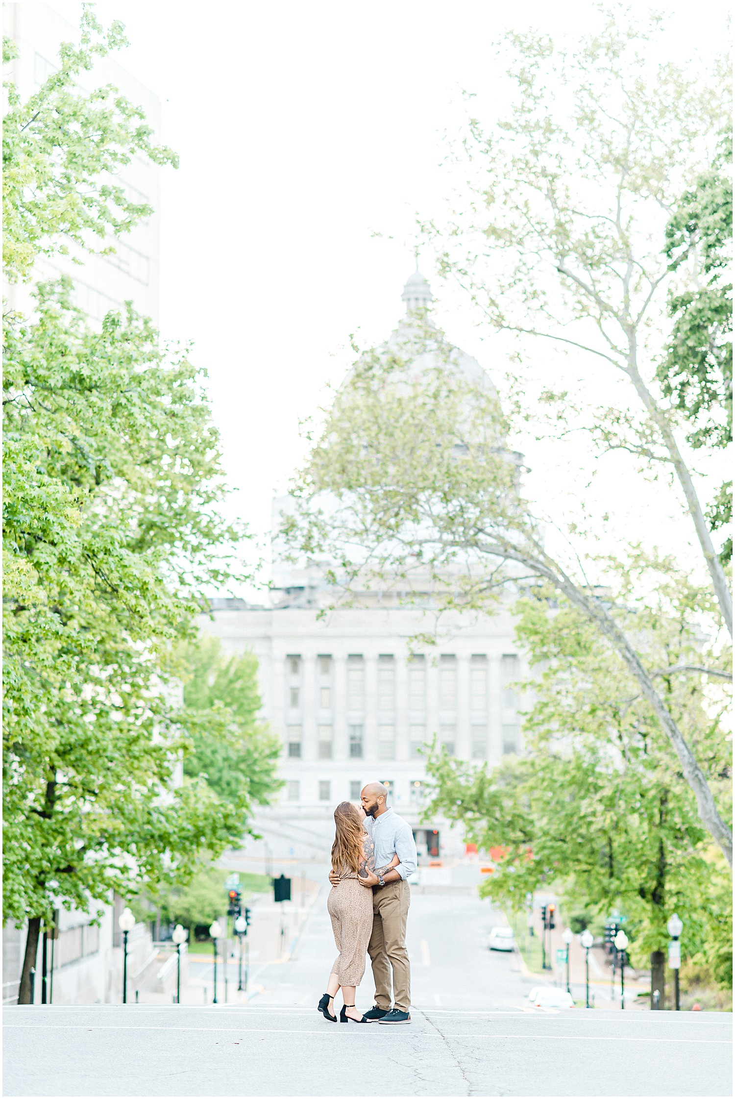 couple kisses in the middle of the street with trees and Missouri state capitol in the background