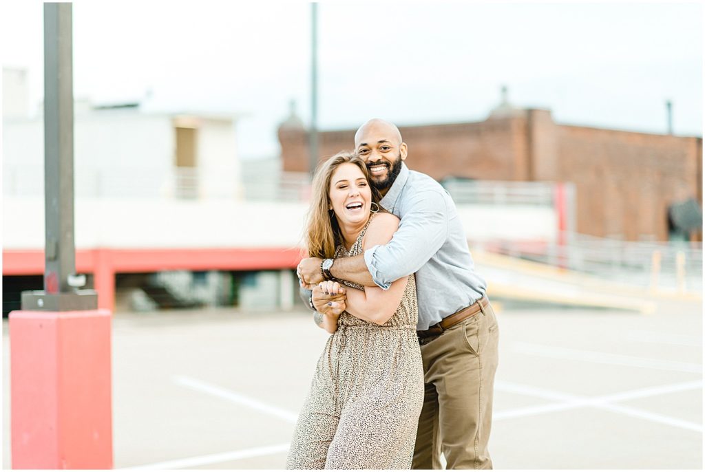 couple laughs and hugs each other on top of parking garage during engagement photos