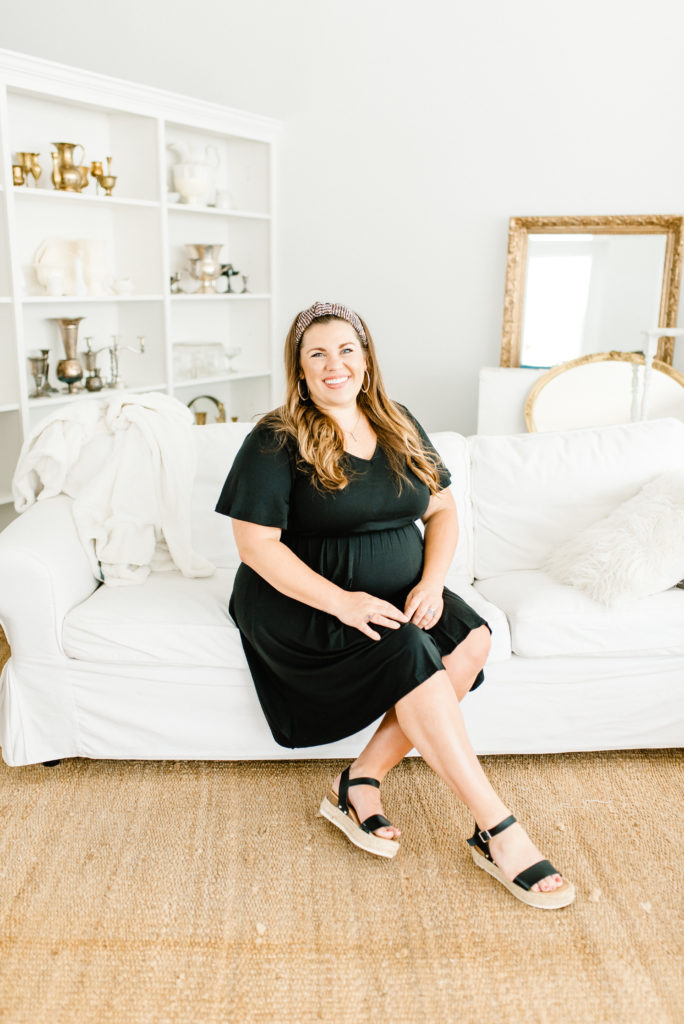 woman in black dress sits on white couch for wedding planner headshots