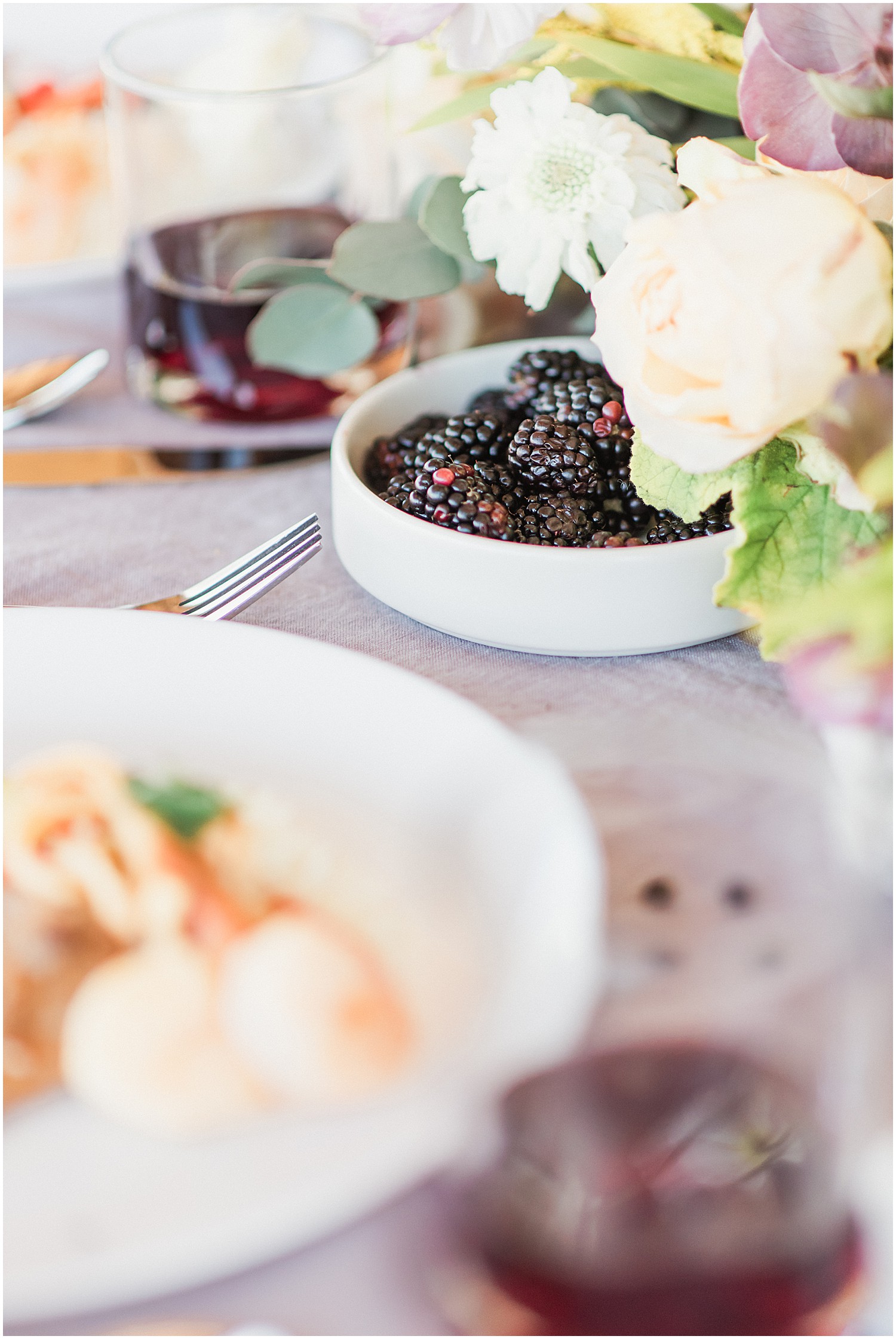 a plate of blackberries sits upon a farm table with a light purple tablecloth