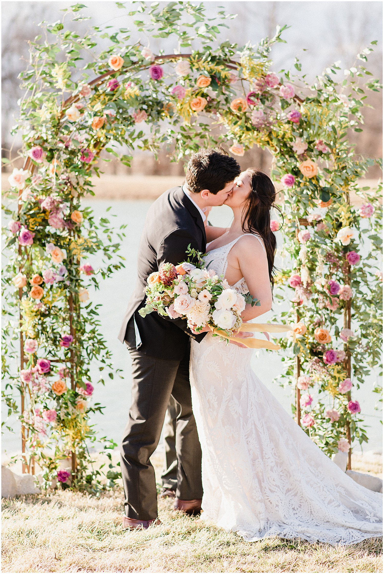 a bride and groom kiss at the alter under a large arch covered in bright florals