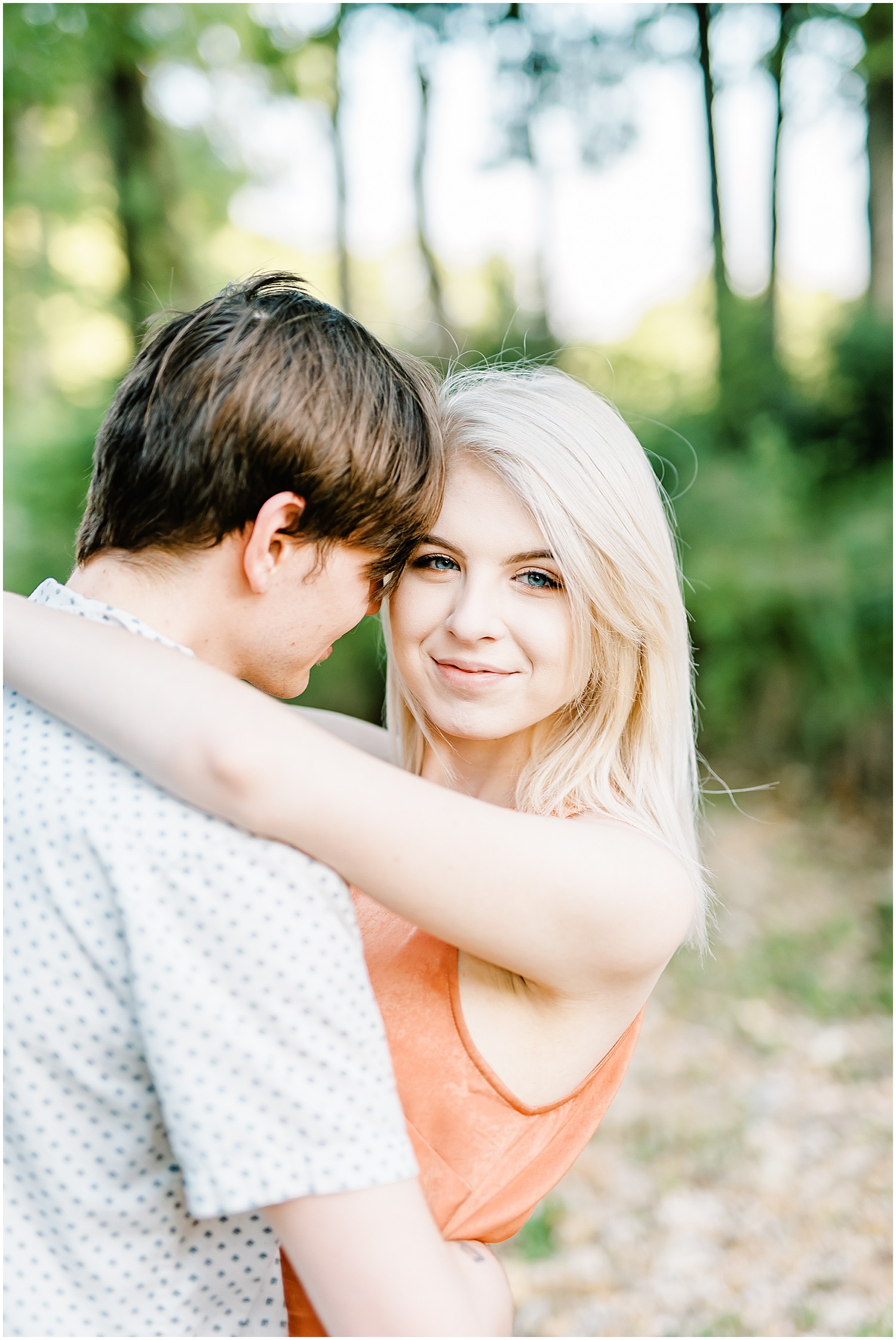 young girl looks over her shoulder at camera while fiancé hugs her for engagement pictures