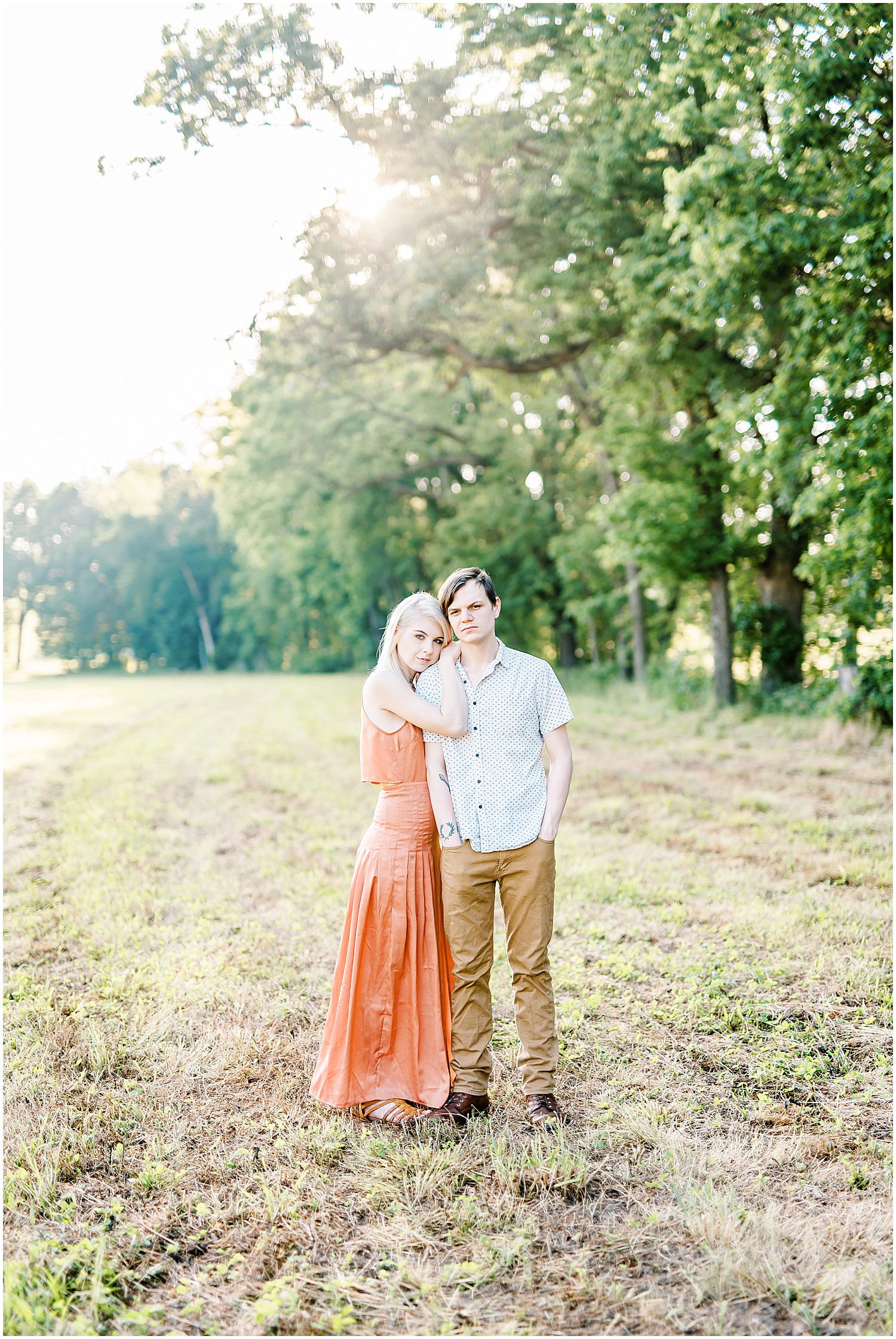 engaged couple stands in field under trees holding each other for kempkers back 40 engagement session in missouri