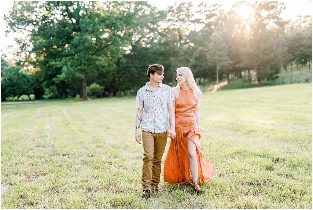 young couple walks through field hand in hand for missouri engagement session