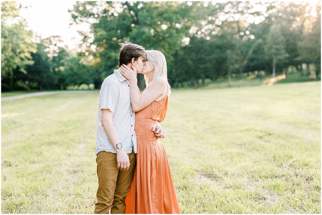 young couple kisses in grassy field for missouri engagement photos