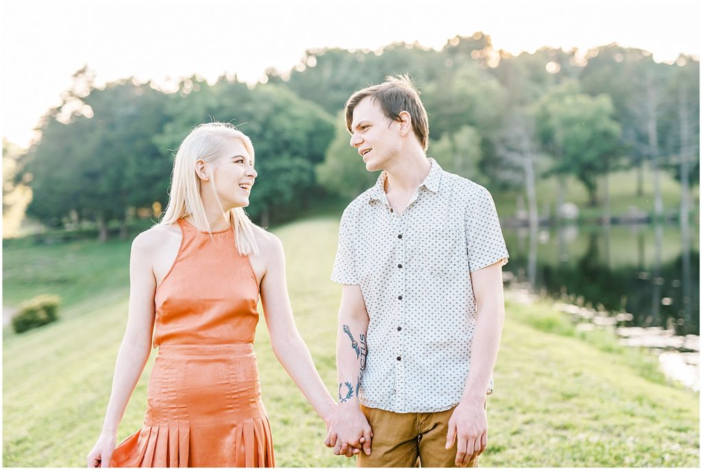 young couple walks holding hands on banks of a lake at kempkers back 40 missouri wedding venue