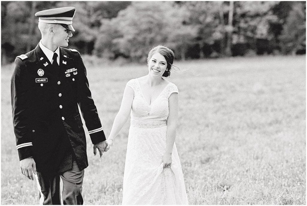 black and white image of bride and groom walking through field on wedding day