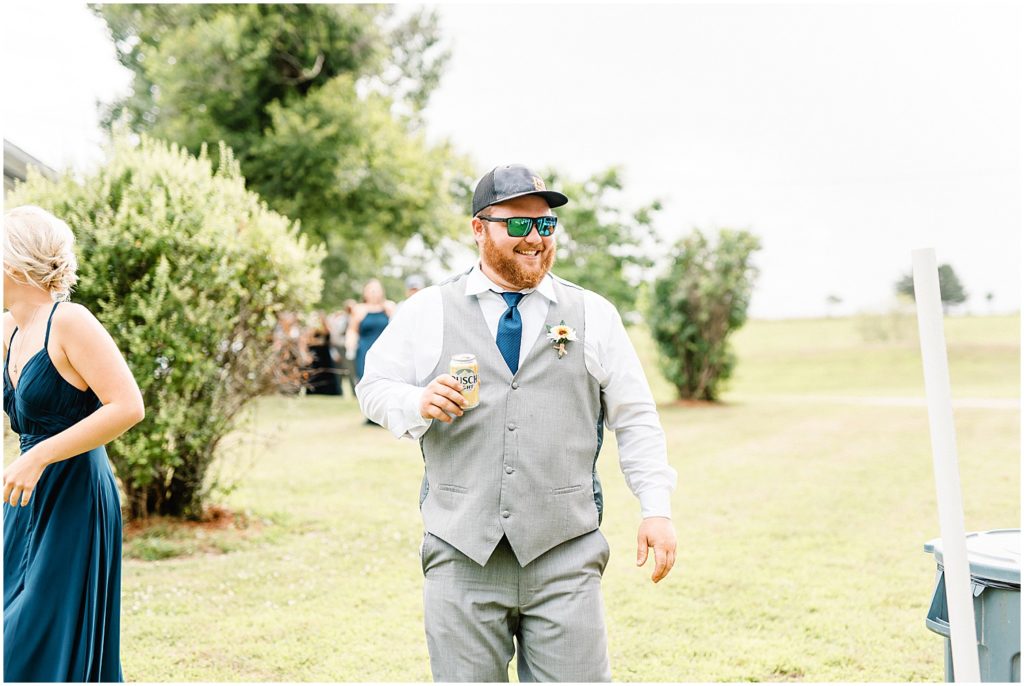 a groomsmen holds a beer and wears sunglasses while entering wedding reception in vienna, mo