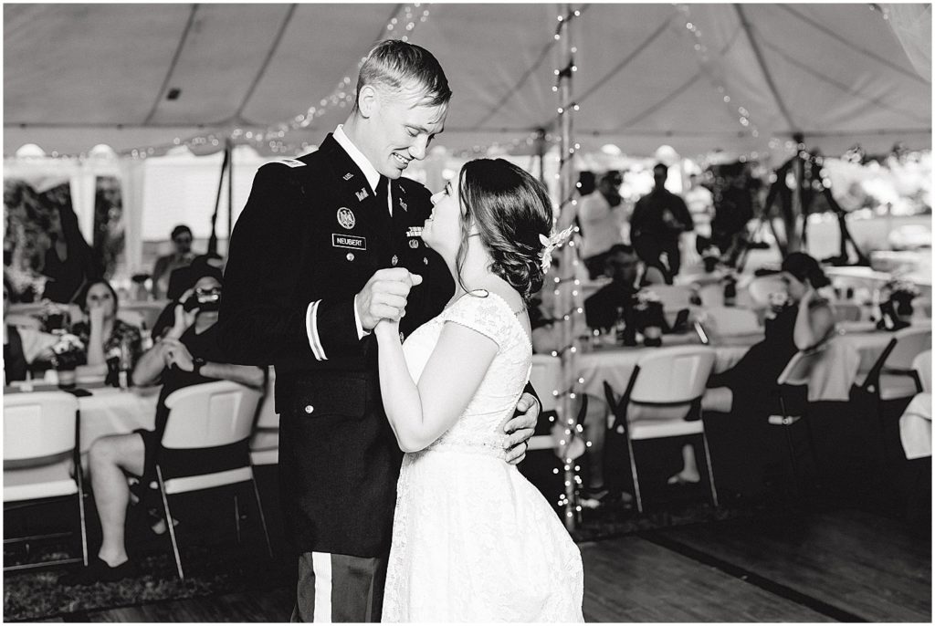 black and white image of bride and groom dancing under large white tent during wedding reception