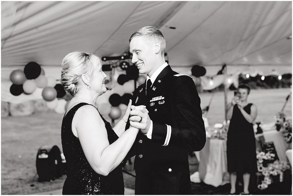 black and white image of groom dancing with his mother at wedding reception under large white tent