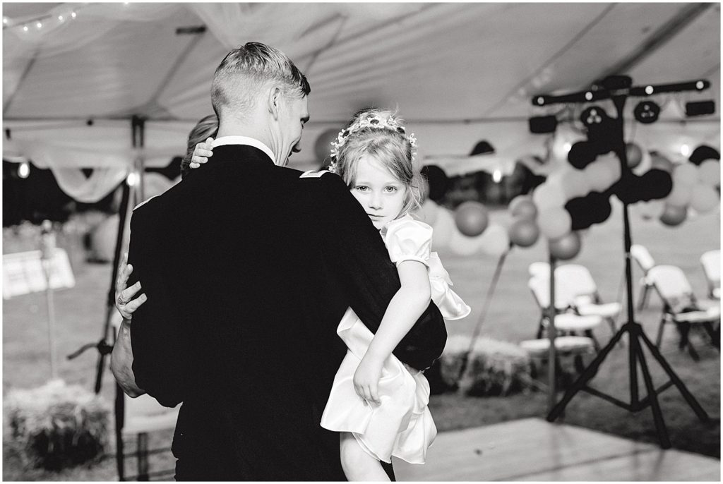 black and white image of groom holding niece while he dances during wedding reception