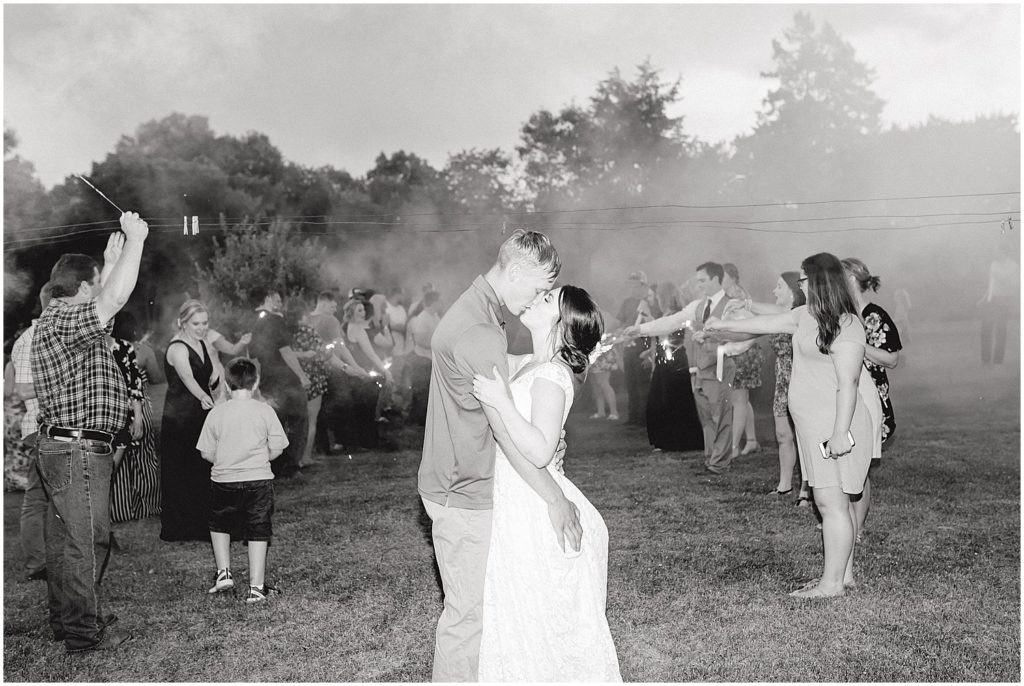 black and white image of bride and groom kissing after sparkler exit during wedding reception in vienna, mo