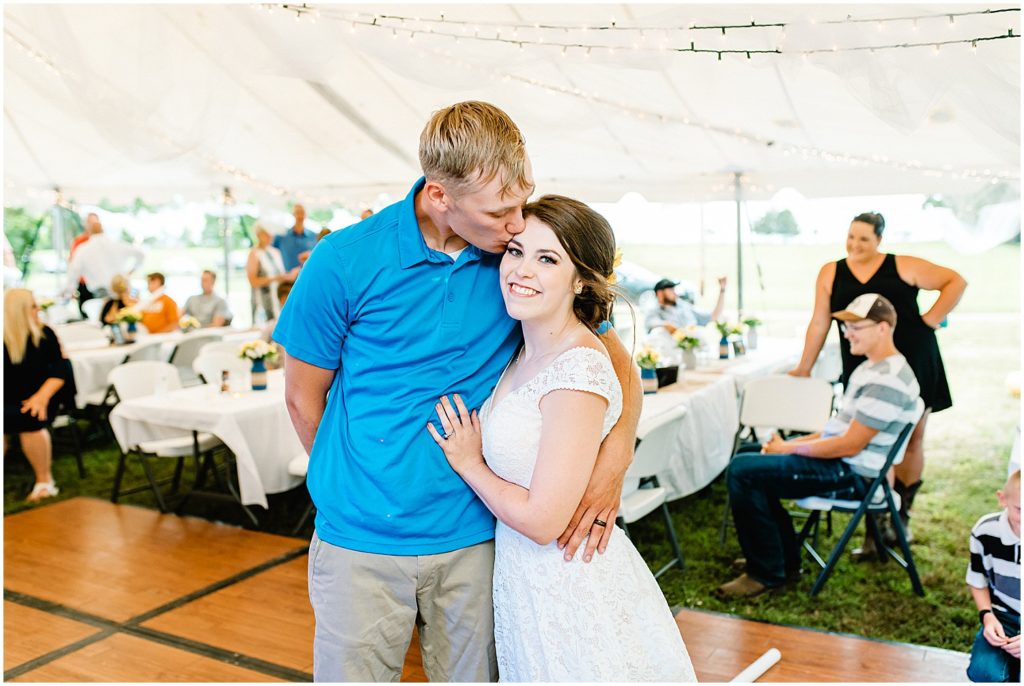 bride and groom kissing under large white tent at wedding reception