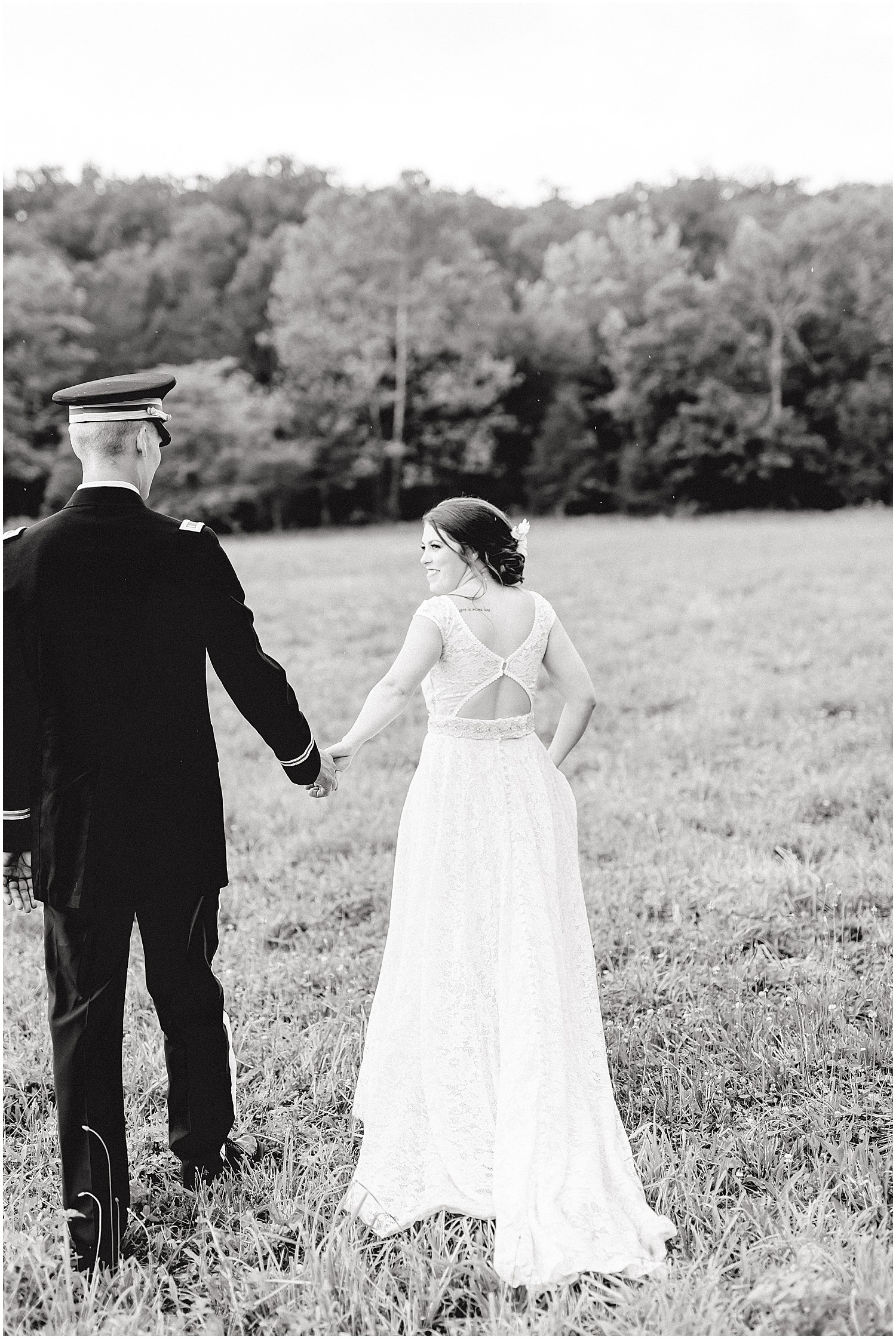 black and white image of bride and groom walking through field on wedding day