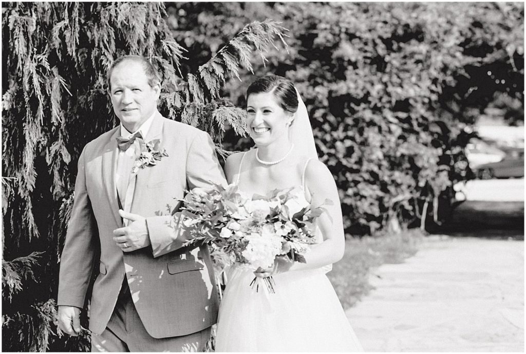 black and white image of bride walking with her father down the ceremony aisle 