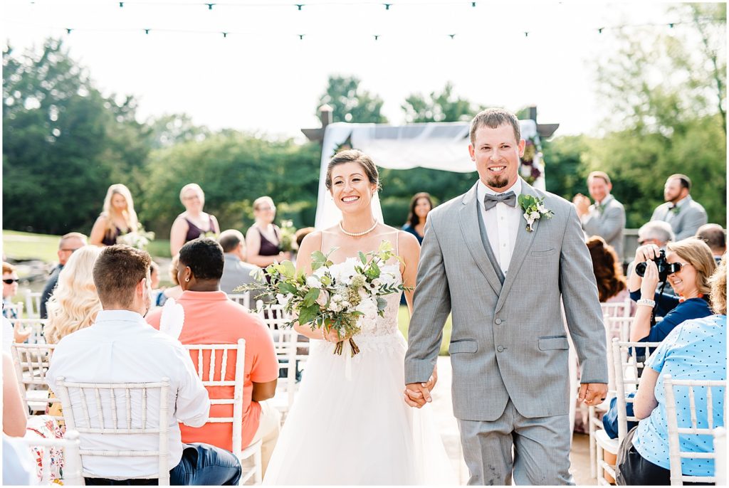 bride and groom smile at guests as they exit cedar lake cellars wedding ceremony