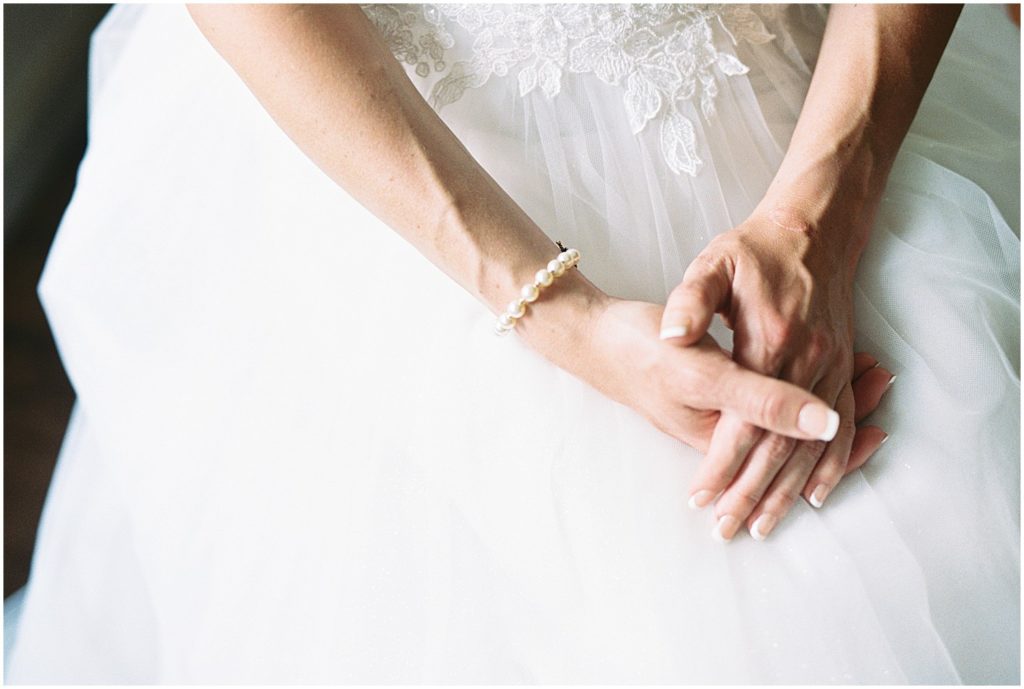a bride's hands rest on her chiffon gown with a pearl bracelet on one wrist