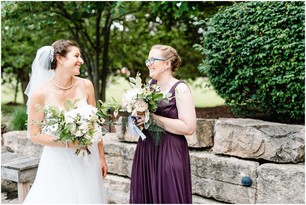 a bride and her maid of honor smile at each other during wedding party portraits