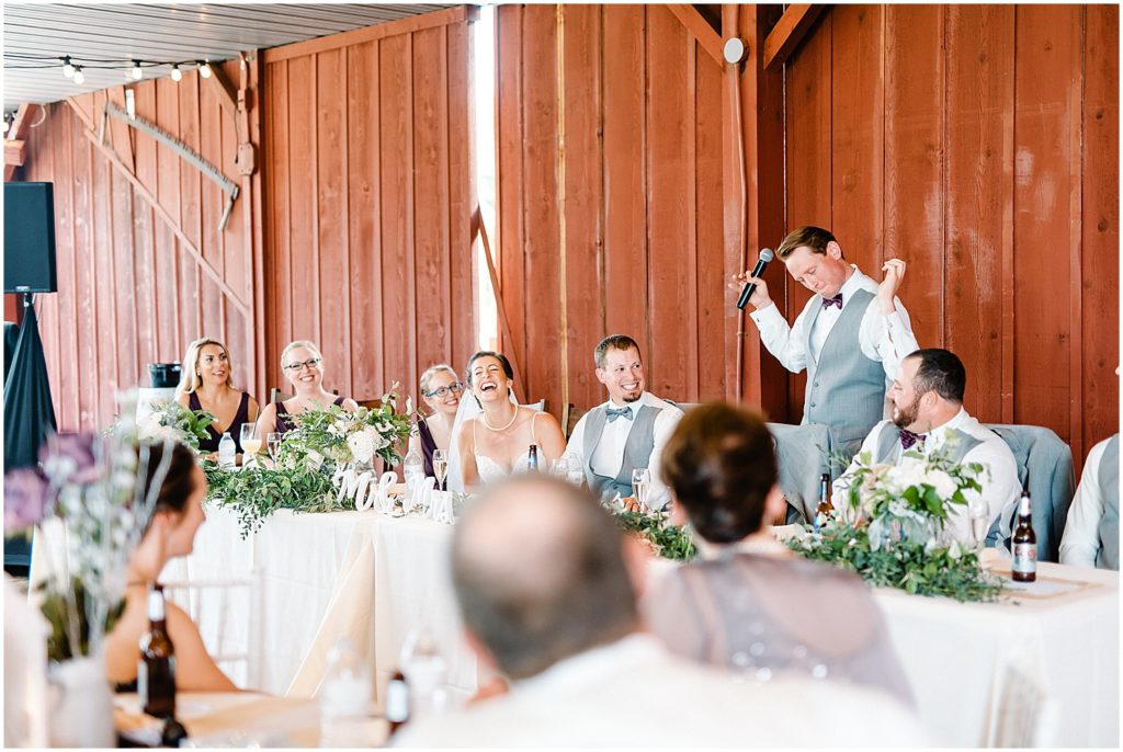 bride and groom laugh as best man gives his speech during wedding reception