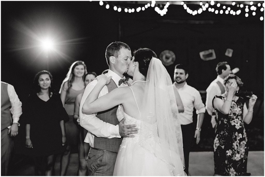 black and white image of bride and groom kissing under the lights during wedding reception on outdoor patio at cedar lake cellars in wright city, mo