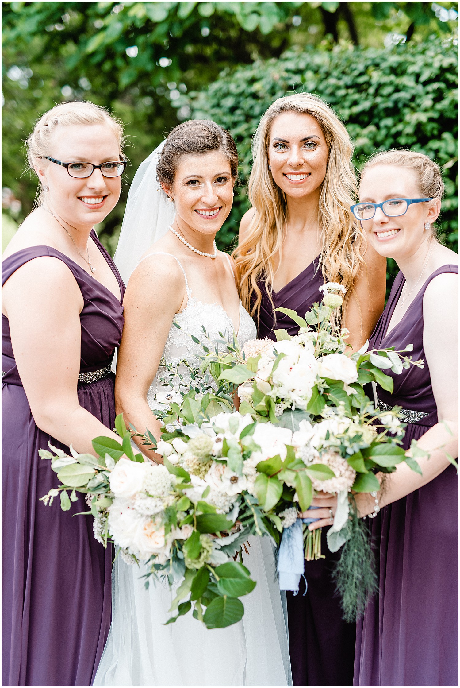 bride and bridesmaids smile at the camera holding green and white bouquets